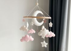 a crib mobile with clouds, stars and a crescent hanging from the ceiling in front of a window