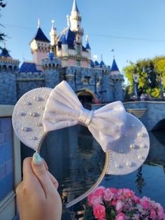 a person holding up a minnie mouse ears in front of a castle with pink flowers