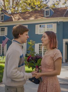 a boy and girl standing in front of a blue house with flowers on their hands