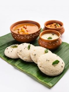 some food is sitting on a green leaf next to bowls of soup and sauces