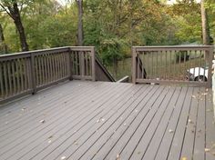 a wooden deck with railings in the middle and trees on both sides that have fallen leaves all over it