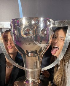 two women sticking their tongues out in front of a trophy