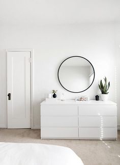 a white dresser with a round mirror above it and plants in pots on the top