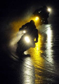 two motorcyclists riding in the rain at night with their headlights turned on