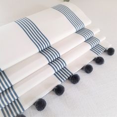 four white and blue striped napkins with pom - poms on them sitting next to each other