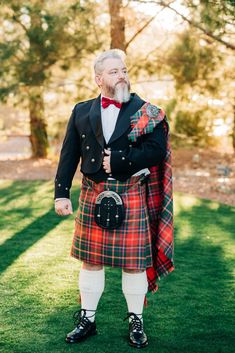 an old man in a kilt standing on the grass with his arms around him