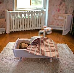 a doll is laying in a toy bed on the floor next to a crib