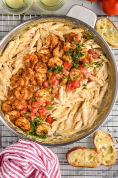 pasta with shrimp and tomatoes in a skillet next to garlic bread on a cooling rack