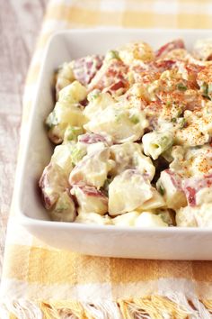 a white bowl filled with potato salad on top of a yellow and white checkered table cloth