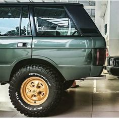 a green suv parked in a garage next to another vehicle with gold rims and tires