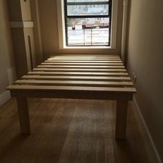 a wooden bed frame sitting in front of a window on top of a hard wood floor