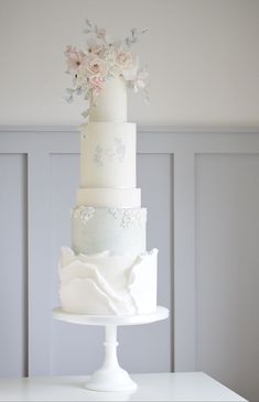 a three tiered wedding cake with flowers on the top and bottom, sitting on a white pedestal