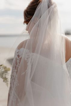 the back of a bride's veil as she walks along the beach with her bouquet