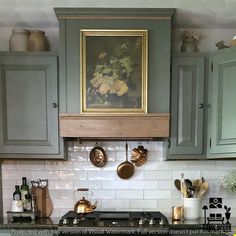 a painting hangs above the stove in a kitchen with green cabinets and white tile backsplash