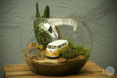 a small bus is in a glass bowl with rocks and succulents inside