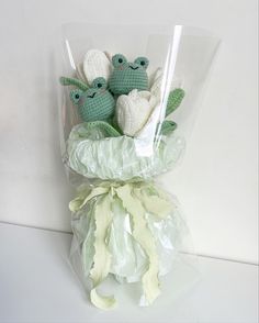 three crocheted green and white stuffed animals in a cellophane wrapped bouquet