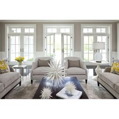 a living room with couches and chairs in front of two large windows, one has yellow flowers on the coffee table