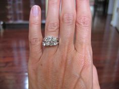 a woman's hand with a diamond ring on top of her finger, in front of a wooden floor