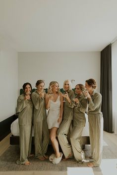 a group of women standing next to each other in front of a bed holding wine glasses