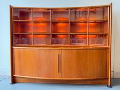 a wooden cabinet with glass doors and shelves on it's sides, in front of a white wall