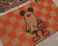 a mickey mouse door mat with a pumpkin on it and a ghost in the background