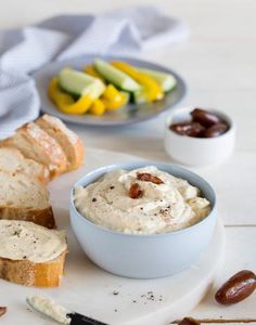 a bowl of cream cheese sits next to bread and olives