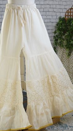 PRODUCT DETAILS Off-White Palazzo Pants with Hexagon gold work on the Shararaa and a gold border. It is beautifully made in soft mul-mul cotton fabric and has a flary hem. It also has an attached lining inside. It has a stretchy elastic band and a tying string for a good fit. The Skirt can fit up to size 42 inch waist and can be tightened with the strings for narrower waist. Size & Fit One Size Waist: 28 (expandable to 42) Height: 39 inches Inseam: 24 inches Color: Off-White Material & C White Palazzo Pants Outfit Indian, Elegant Long Skirt For Festive Occasions, Elegant Festive Long Skirt, Elegant Gold Wedding Bottoms, Fitted Gold Bottoms For Wedding, Gold Fitted Bottoms For Wedding, Gold Festive Wedding Pants, Traditional Gold Pants For Festive Occasion, Elegant Fitted Bottoms For Festivals