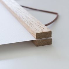 a close up of a piece of wood on top of a white surface with a brown cord