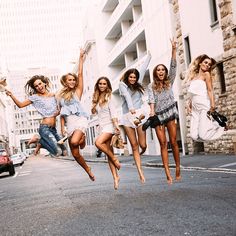 a group of young women jumping in the air while wearing skirts and tops on a city street