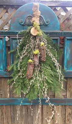 a wreath hanging on the side of a wooden fence with pine cones and greenery