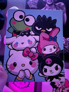 a person holding up a painting with hello kitty on it's face and other cartoon characters