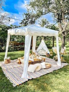 a white canopy bed sitting on top of a grass covered field next to a picnic table