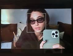 a woman in sunglasses holding up a cell phone