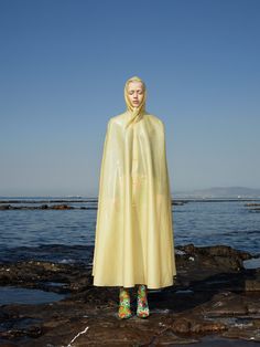 a woman standing on top of a rocky beach wearing a yellow raincoat and rubber boots