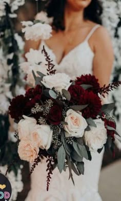 a bride holding a bouquet of red and white flowers with greenery around her neck