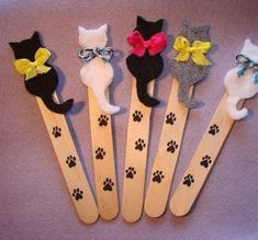 six wooden cat utensils with bows and paws on them, all decorated in different colors