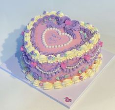 a heart - shaped cake is decorated with pastel icing and flowers on a white surface