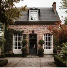 an old brick house with potted plants in the front yard and two large windows