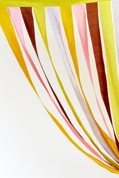 an orange vase with flowers in it sitting under a colorful striped cloth draped from the ceiling