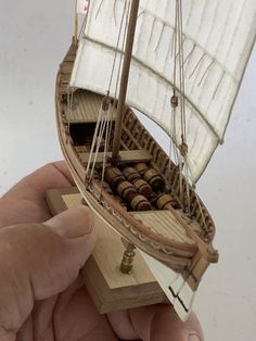 a hand holding a small model sailboat in it's right hand, with the sails down