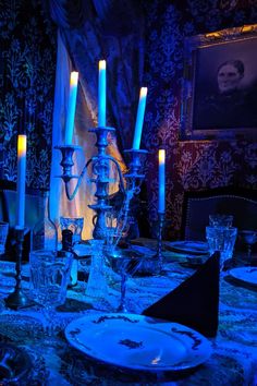 a dining room table set with candles and plates in blue lighting up the wall behind it