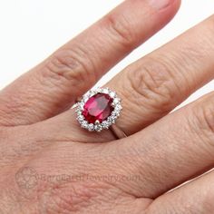 a woman's engagement ring with a large red stone surrounded by small white diamonds