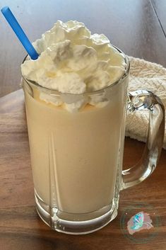 a glass mug filled with whipped cream on top of a wooden table