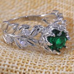 a ring with green and white stones on it sitting on top of a table cloth