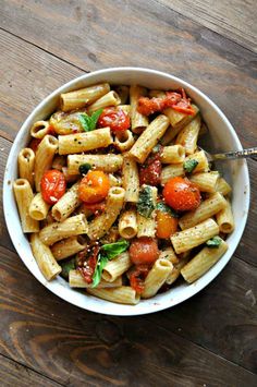 a bowl filled with pasta and tomatoes on top of a wooden table next to a fork