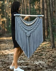 a woman is carrying a large piece of cloth in the woods with beads on it