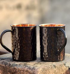 two black coffee mugs sitting next to each other on a stone slab in front of a building