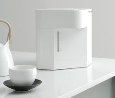 a white coffee pot sitting on top of a counter next to a cup and saucer