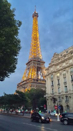 the eiffel tower lit up at night with cars passing by in front of it