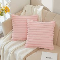 two pink pillows sitting on top of a couch next to a vase with yellow flowers